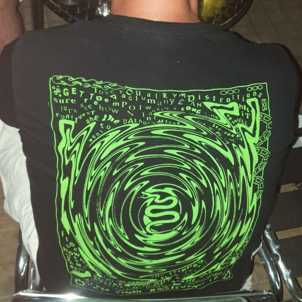 Person wearing a black t-shirt with a green spiral design, sitting at a table.