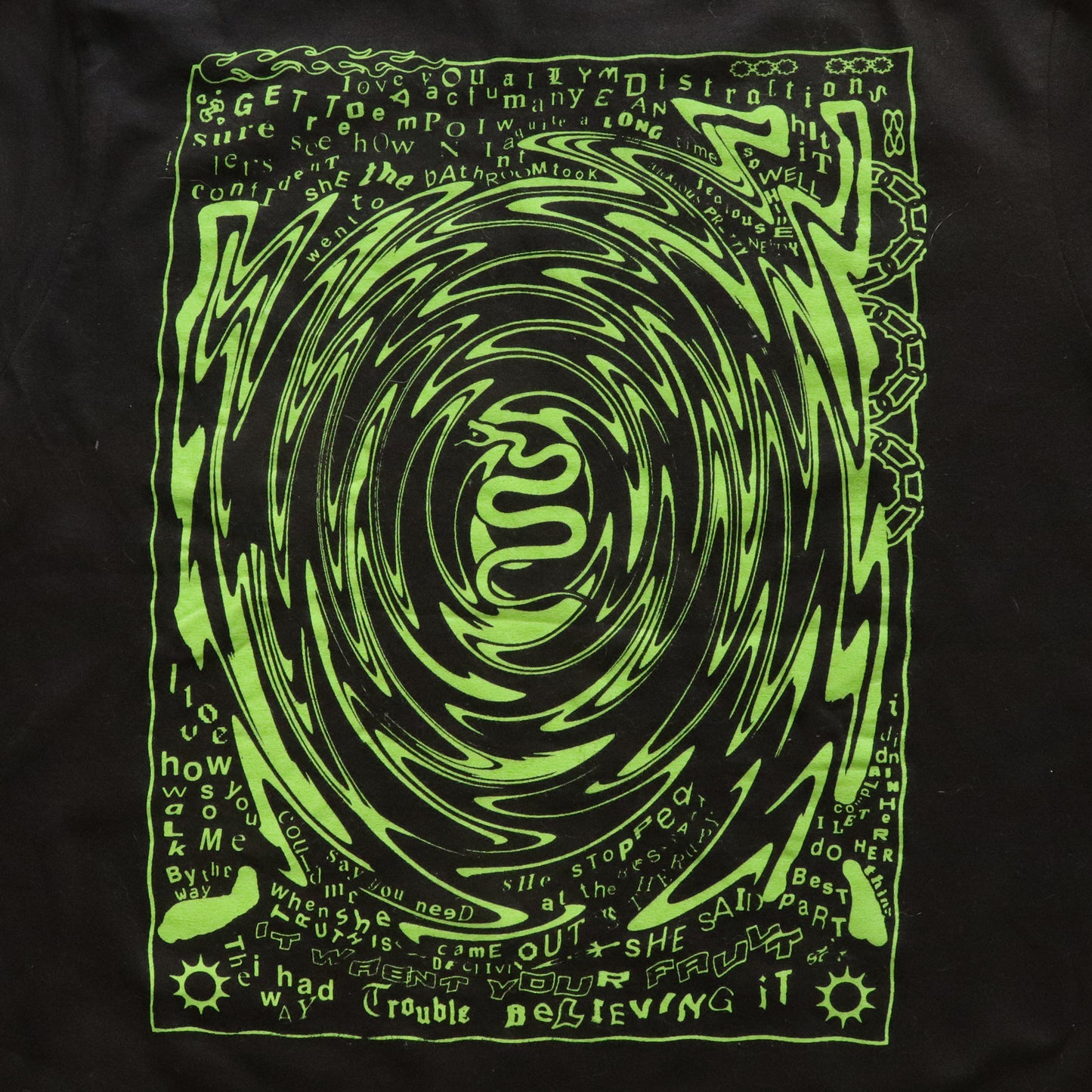 Close-up view of black t-shirt featuring a neon green hand screen-printed design with swirling artwork and handwritten lyrics from the song ‘FILTH’ on the back.