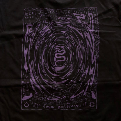 Close-up of Black t-shirt featuring a purple hand screen-printed design with swirling artwork and handwritten lyrics from the song ‘FILTH’ on the back.”
