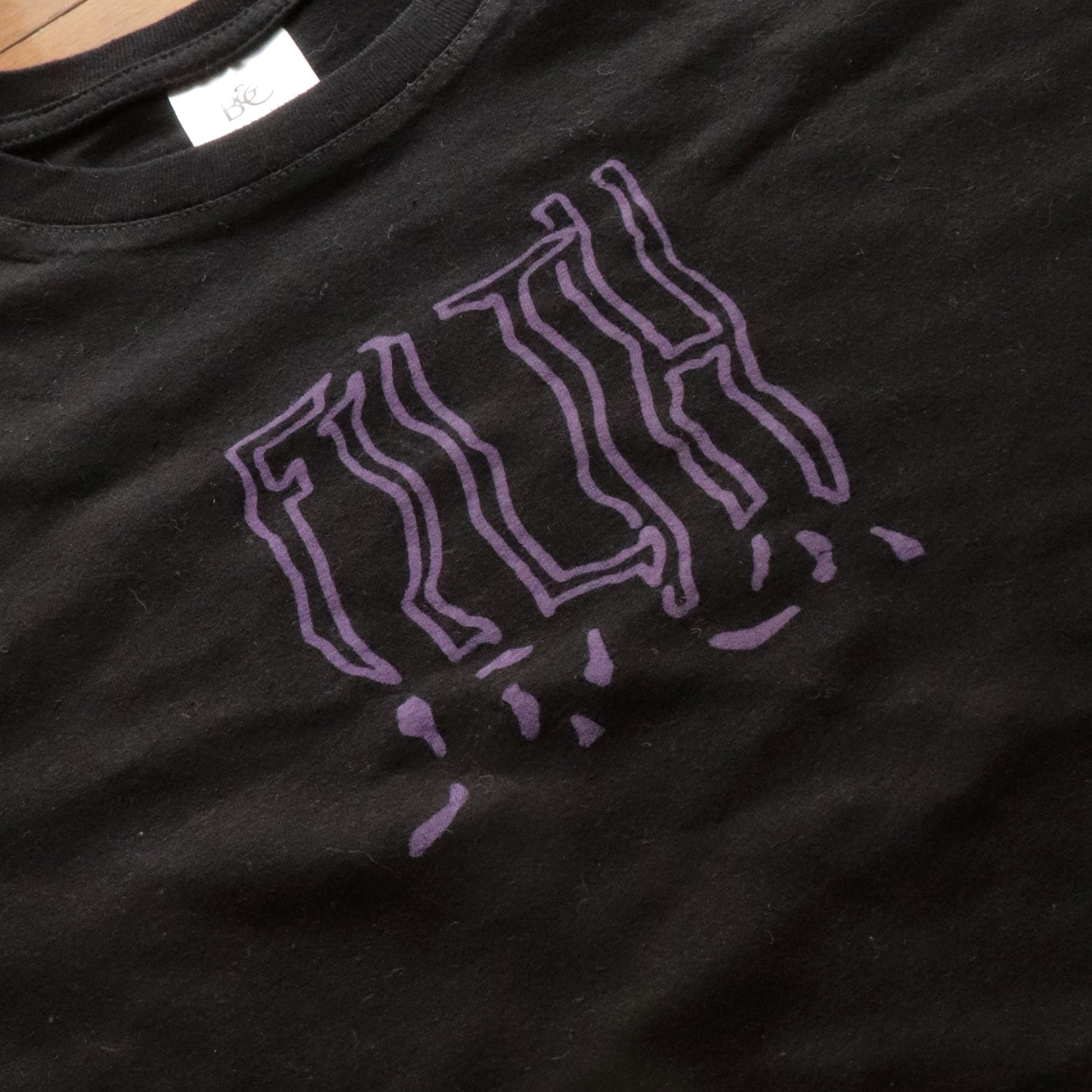 Close-up view of black t-shirt with hand screen printed FILTH in purple bold lettering.