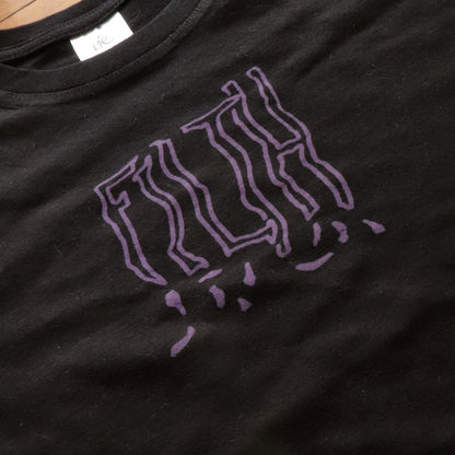 Close-up view of black t-shirt with hand screen printed FILTH in purple bold lettering.