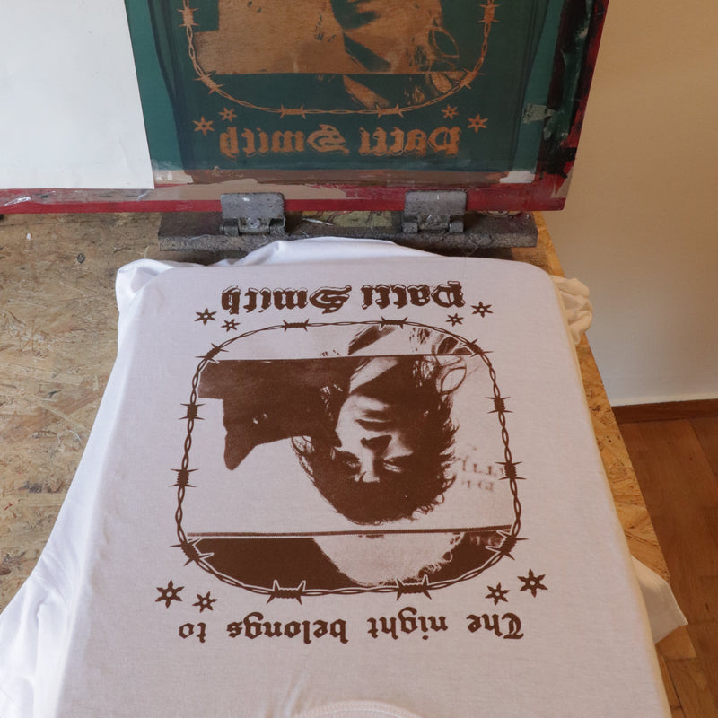 T-shirt and book with a silhouette of a woman and text 'The night belongs to Patti Smith' on a wooden surface.