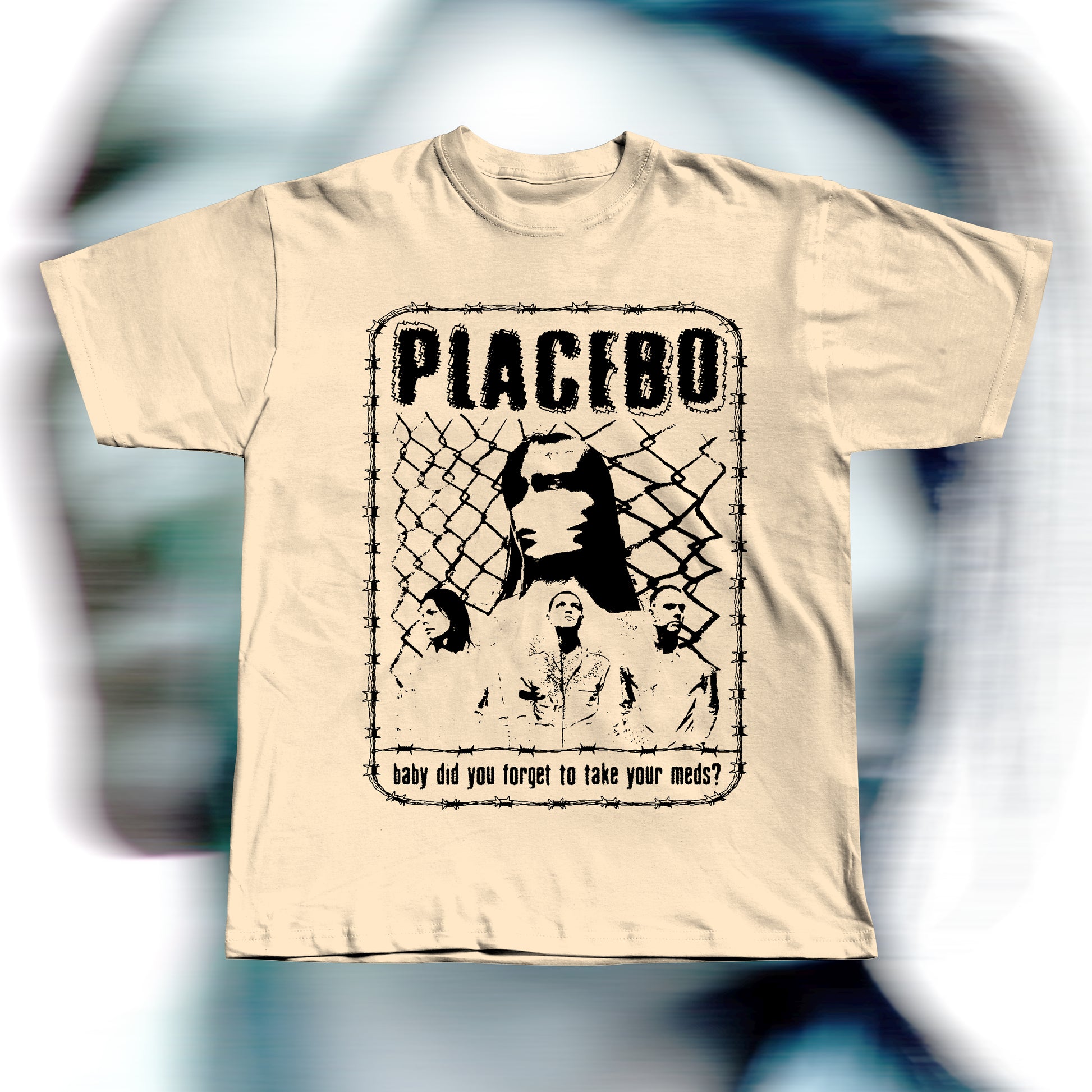 Handmade beige t-shirt featuring purple screen-printed fan art inspired by Placebo. The design shows the band members in front of a chain-link fence with “PLACEBO” written in bold distressed letters and the lyric “baby did you forget to take your meds?” below, surrounded by a barbed-wire border.