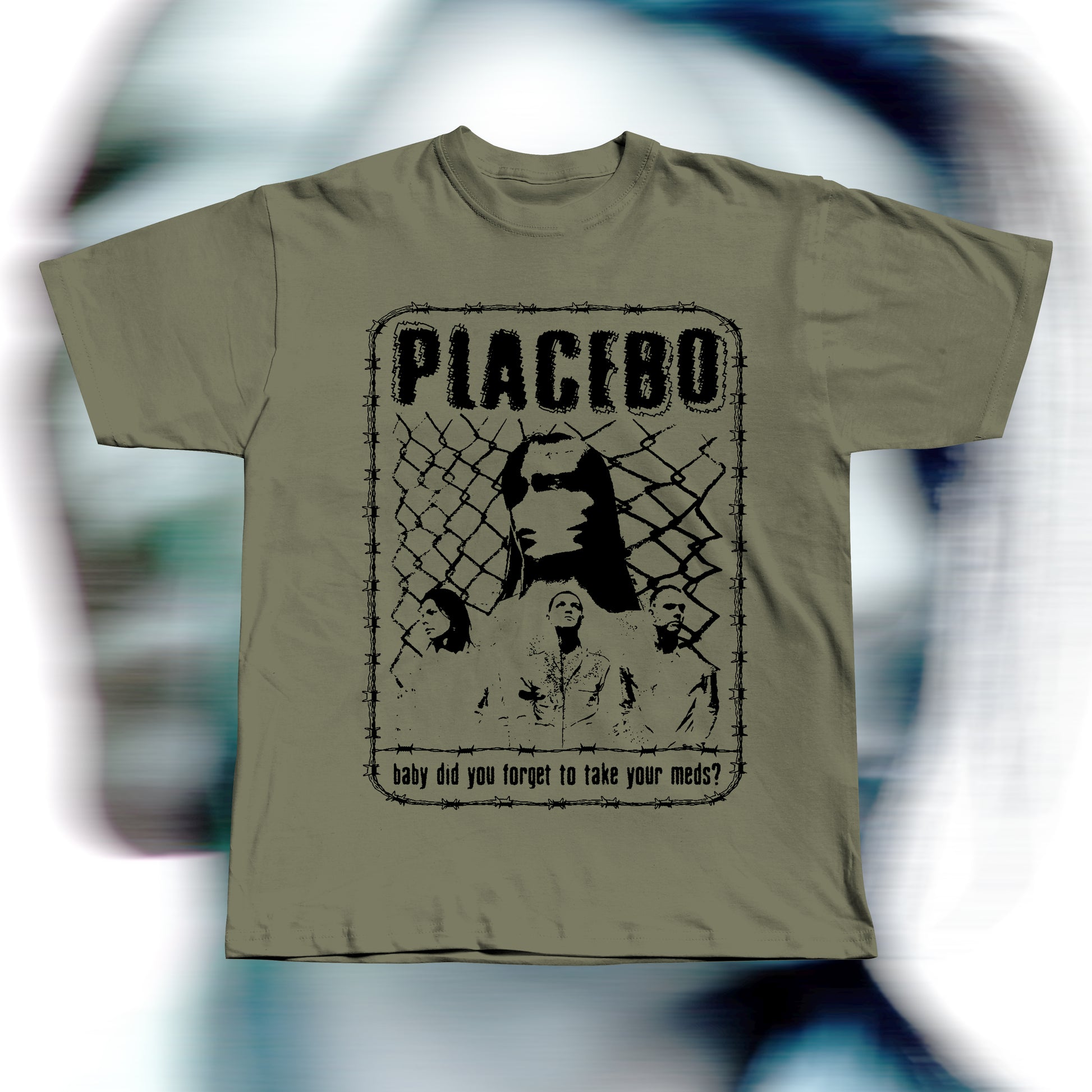 Handmade khaki t-shirt featuring purple screen-printed fan art inspired by Placebo. The design shows the band members in front of a chain-link fence with “PLACEBO” written in bold distressed letters and the lyric “baby did you forget to take your meds?” below, surrounded by a barbed-wire border.