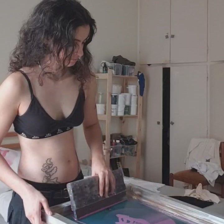 Person holding a screen printing frame with ink on a table in a room.