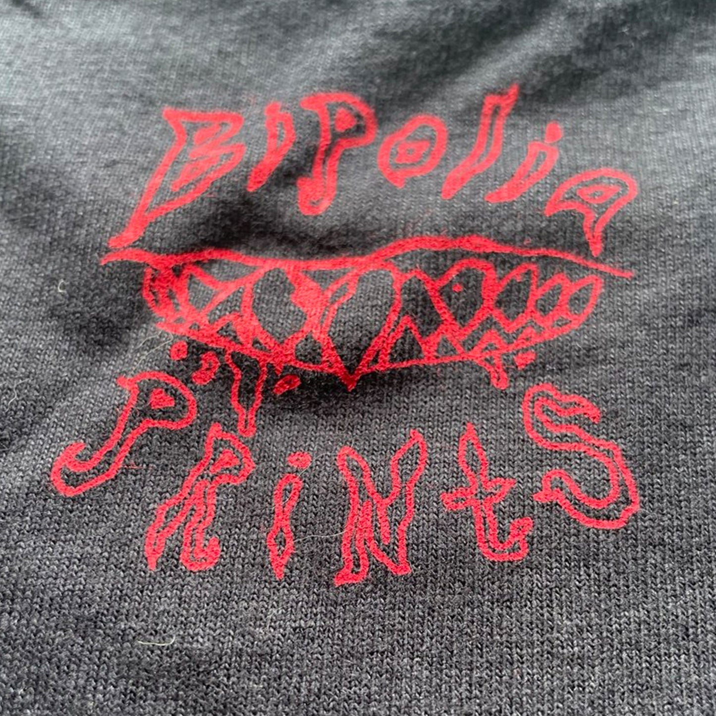 Close up of BIPOLIAPRINTS logo and teeth sketch on the back of the cropped shirt, featuring a minimalist edgy graphic across the chest.