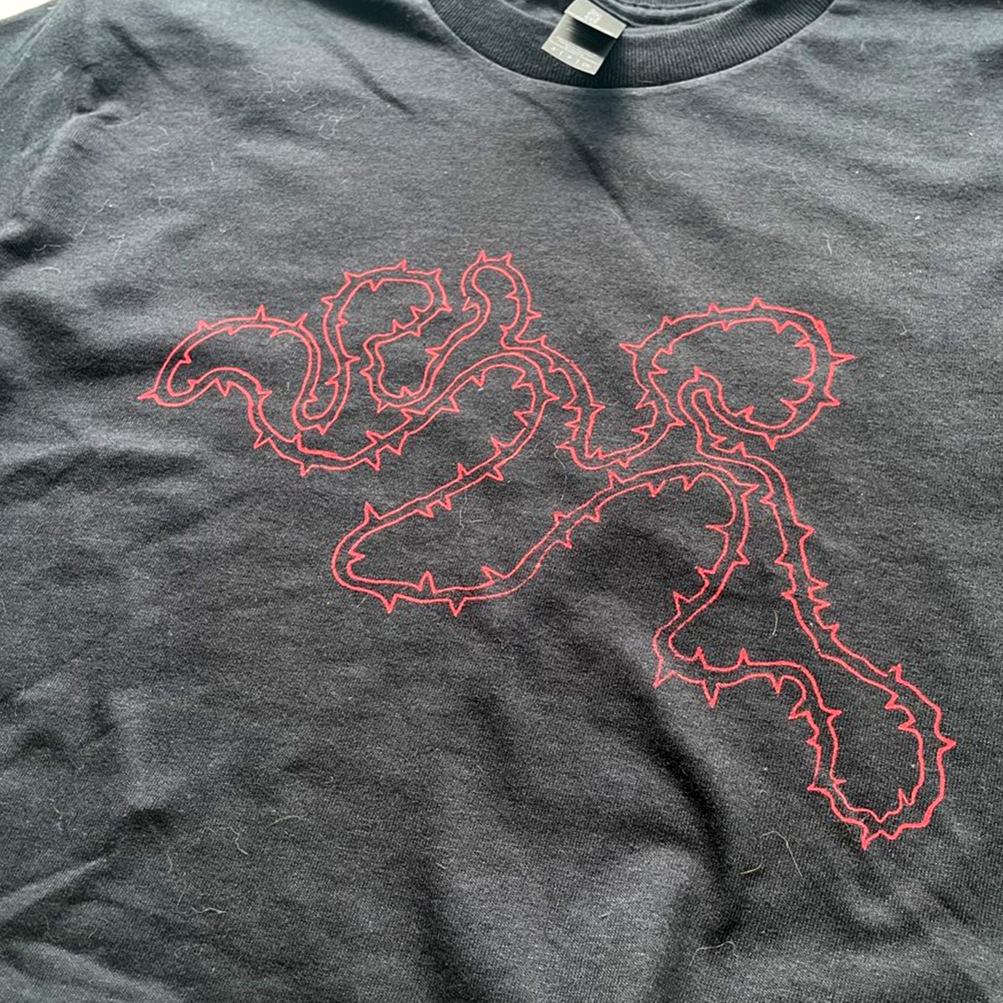 Close up of black cropped t-shirt with red thorny abstract line design, featuring a minimalist edgy graphic across the chest.