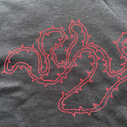 Close up of black cropped t-shirt with red thorny abstract line design, featuring a minimalist edgy graphic across the chest.