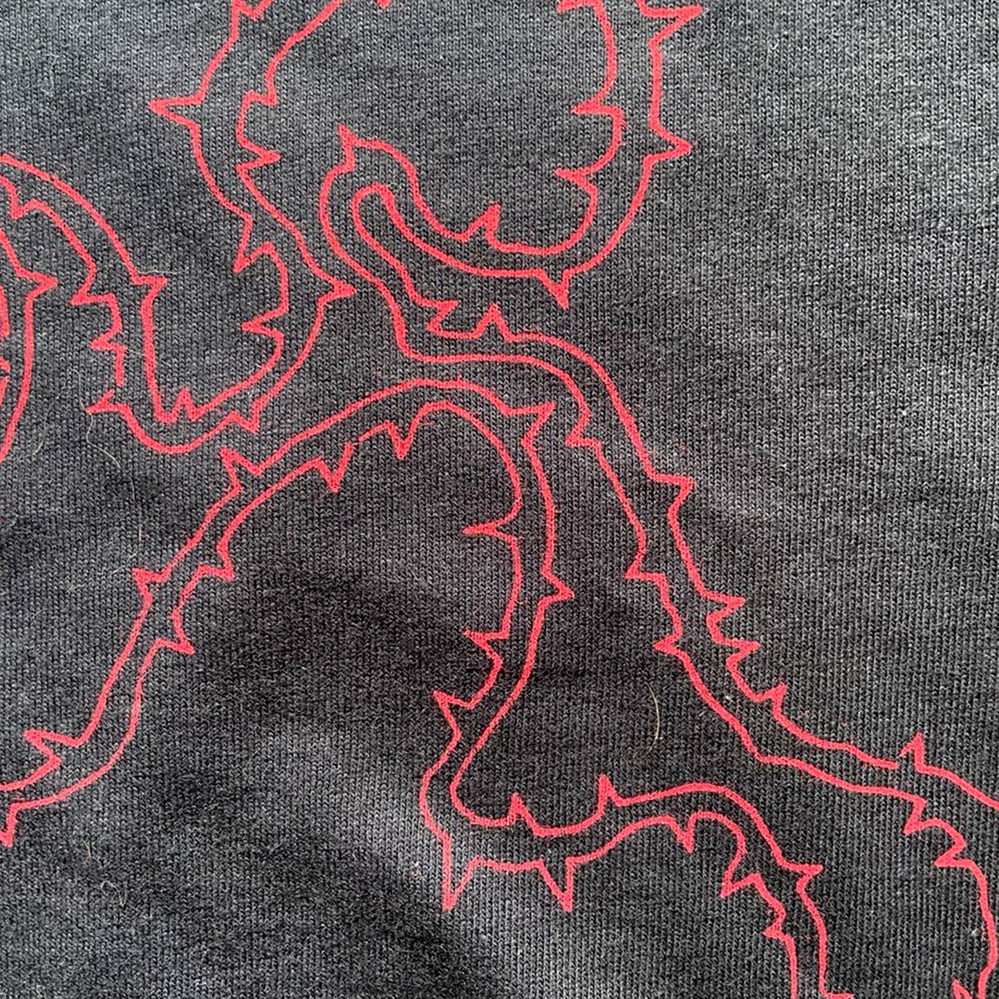 Close up of black cropped t-shirt with red thorny abstract line design, featuring a minimalist edgy graphic across the chest.