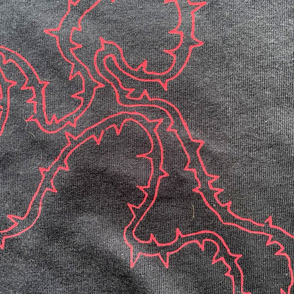 Close up of black cropped t-shirt with red thorny abstract line design, featuring a minimalist edgy graphic across the chest.