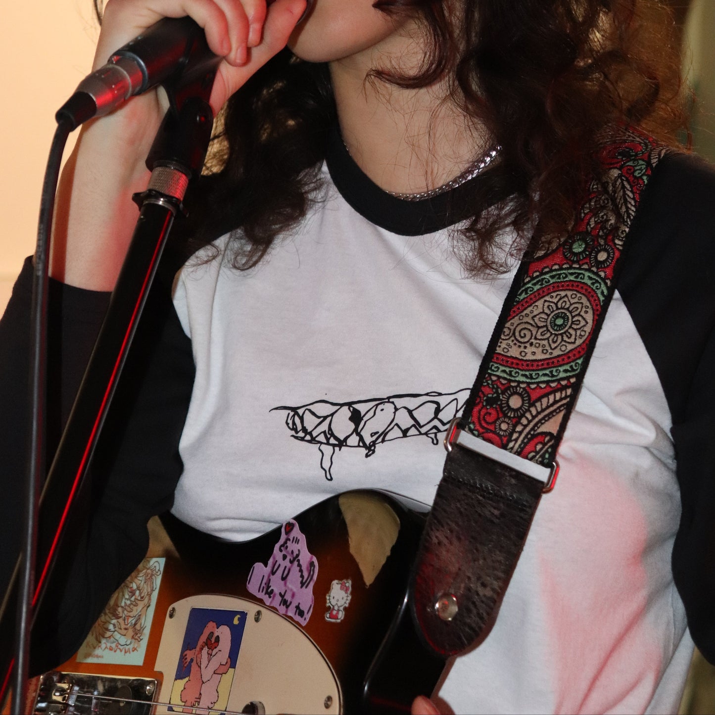 Person playing guitar with a microphone, wearing a white shirt with black design.